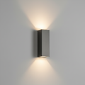 A modern rectangular wall sconce with a brushed dark gray metal finish, mounted on a light gray wall and casting a warm, symmetrical light beam upwards and downwards.