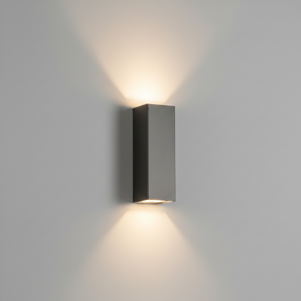 A modern rectangular wall sconce with a brushed dark gray metal finish, mounted on a light gray wall and casting a warm, symmetrical light beam upwards and downwards.